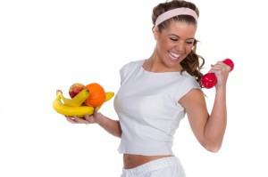 Lachende junge Frau mit Früchten und einer roten Hantel trainie